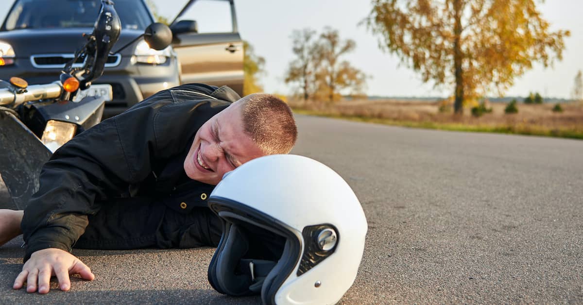 injured motorcyclist lying on road in pain after motorcycle accident with another vehicle