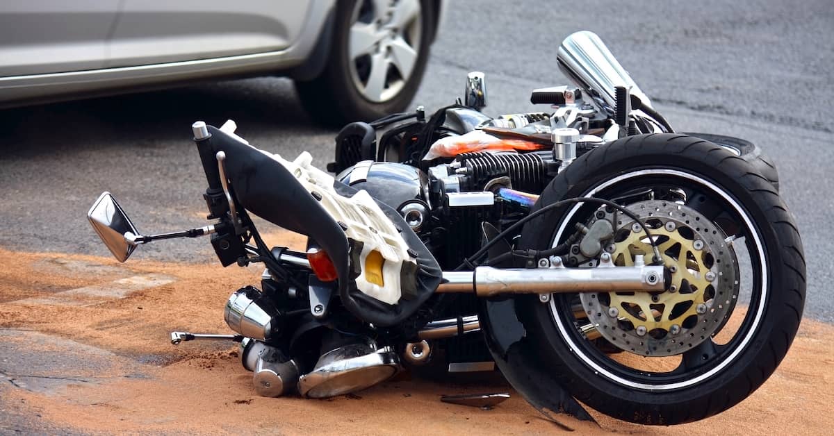 crashed motorcycle on its side next to a car after an accident