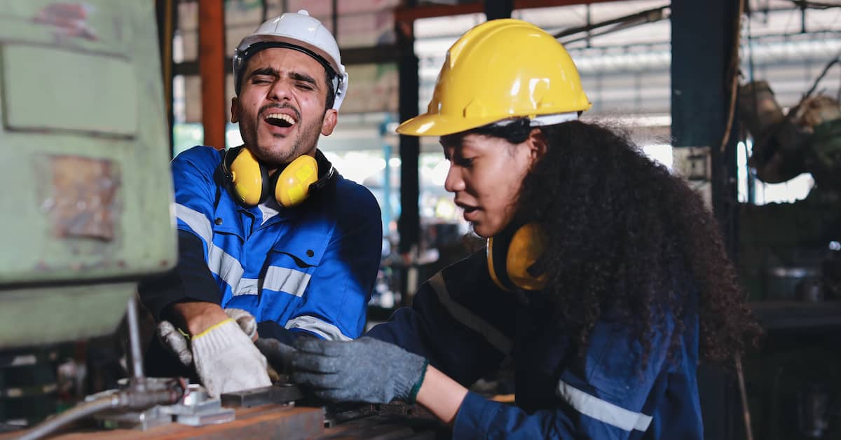 female worker helping male coworker whose hand is stuck in a machine