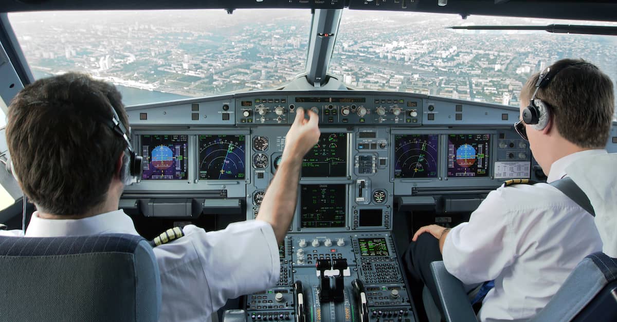 pilot and copilot in the cockpit of a plane on approach to a city