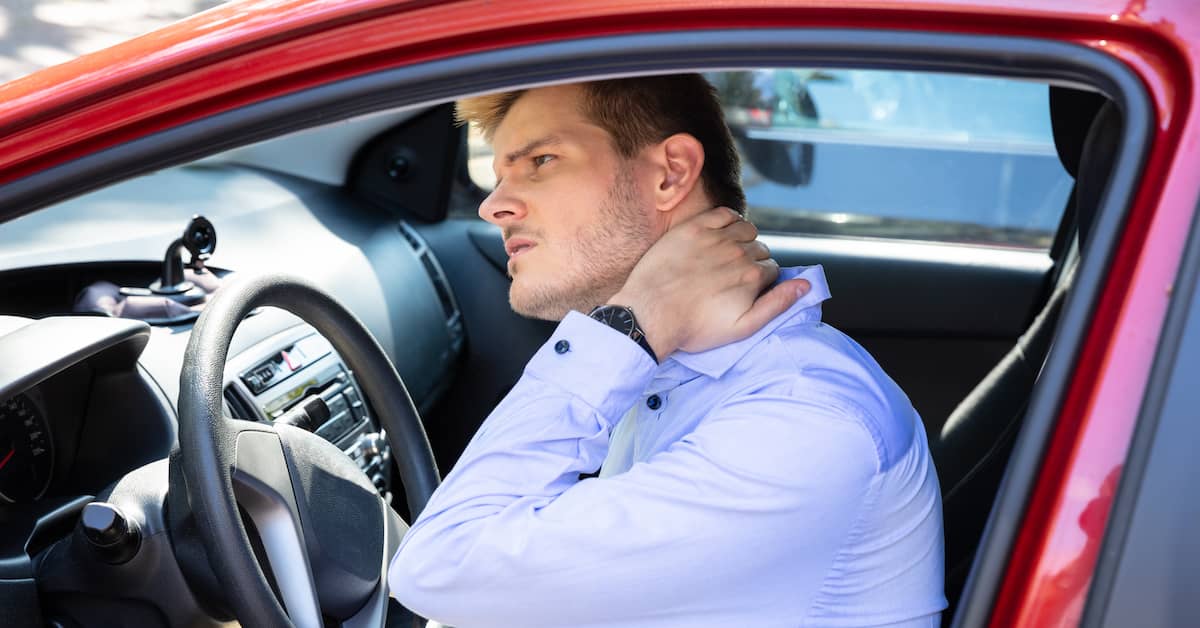 young man sitting in his car rubbing his neck after whiplash injury