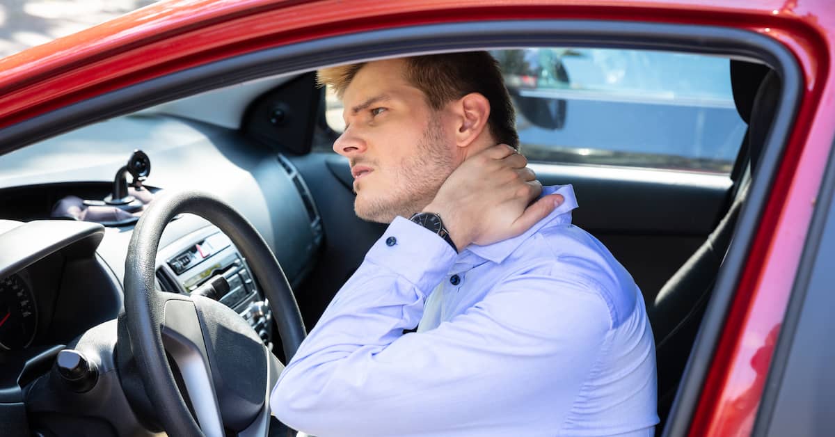 Young man in car rubs his neck after whiplash injury. | Patrick Daniel Law